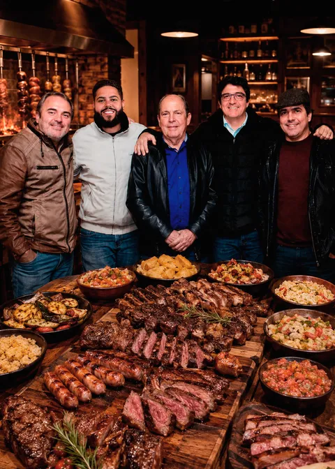 Sr. Antenor com os quatro filhos diante de uma mesa farta de cortes na brasa e guarnições